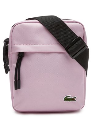 Petit sac bandoulière rose clair avec sangle noire réglable, poche avant zippée et logo crocodile vert dans le coin inférieur droit.