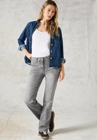 Denim shirt, donkerblauw met knopen aan de voorkant, gedragen over een witte tanktop. Grijze jeans met een slim fit en een licht vervaagd textuur. Zwarte sneakers.