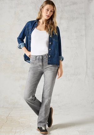 Denim shirt, donkerblauw met knopen aan de voorkant, gedragen over een witte tanktop. Grijze jeans met een slim fit en een licht vervaagd textuur. Zwarte sneakers.