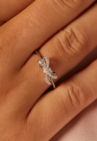Zilveren ring met een vlinderontwerp, met sprankelende accenten en een gladde band. Geplaatst tegen een textuur van de huid.
