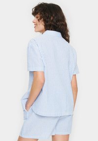 Camicia a maniche corte a righe blu e bianche con colletto, realizzata in tessuto leggero; abbinata a shorts coordinate, dotati di tasche laterali.