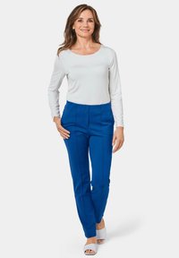 Witte lange mouw top gecombineerd met felblauwe broek met verticale naden. Model draagt witte open-teen hakken.