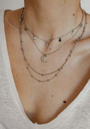 Silbernes mehrlagiges Halsketten-Set mit Ketten, die Sterne und Halbmond-Anhänger, runde Perlen und unterschiedliche Längen aufweisen. Strukturierte Metalloberfläche.