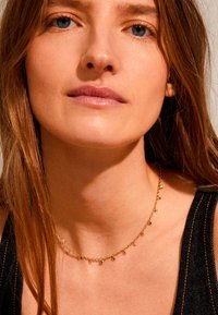 Goldkette mit kleinen, hängenden Charms. Die Kette ist zart und hat eine glatte Textur, die ein einfaches Design ergänzt.