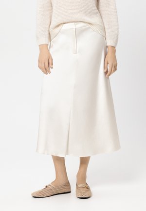 Satinweißes Midikleid mit glatter Textur und ausgestellter Form, mit einem seitlichen Schlitz und einem dezenten Bund, kombiniert mit beigen Ballerinas.