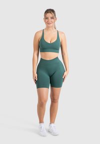 Set sportivo verde composto da un reggiseno con spalline larghe e pantaloni corti a vita alta, realizzato in tessuto morbido con un design aderente.