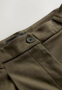 Oliivrohelised püksid, millel on sile kangatekstuur, õmmeldud vöökoht, must sisemärgis ja üks tume nööp kinnituseks.