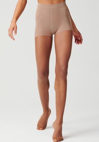 Pantaloni corti elasticizzati beige con una texture liscia, dotati di un elastico in vita e di lunghezza a metà coscia, indossati con collant trasparenti.