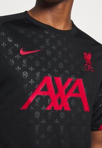 Černý fotbalový dres s krátkým rukávem s texturovaným vzorem, s červeným logem Nike, výrazným nápisem "AXA" a znakem Liverpool FC.