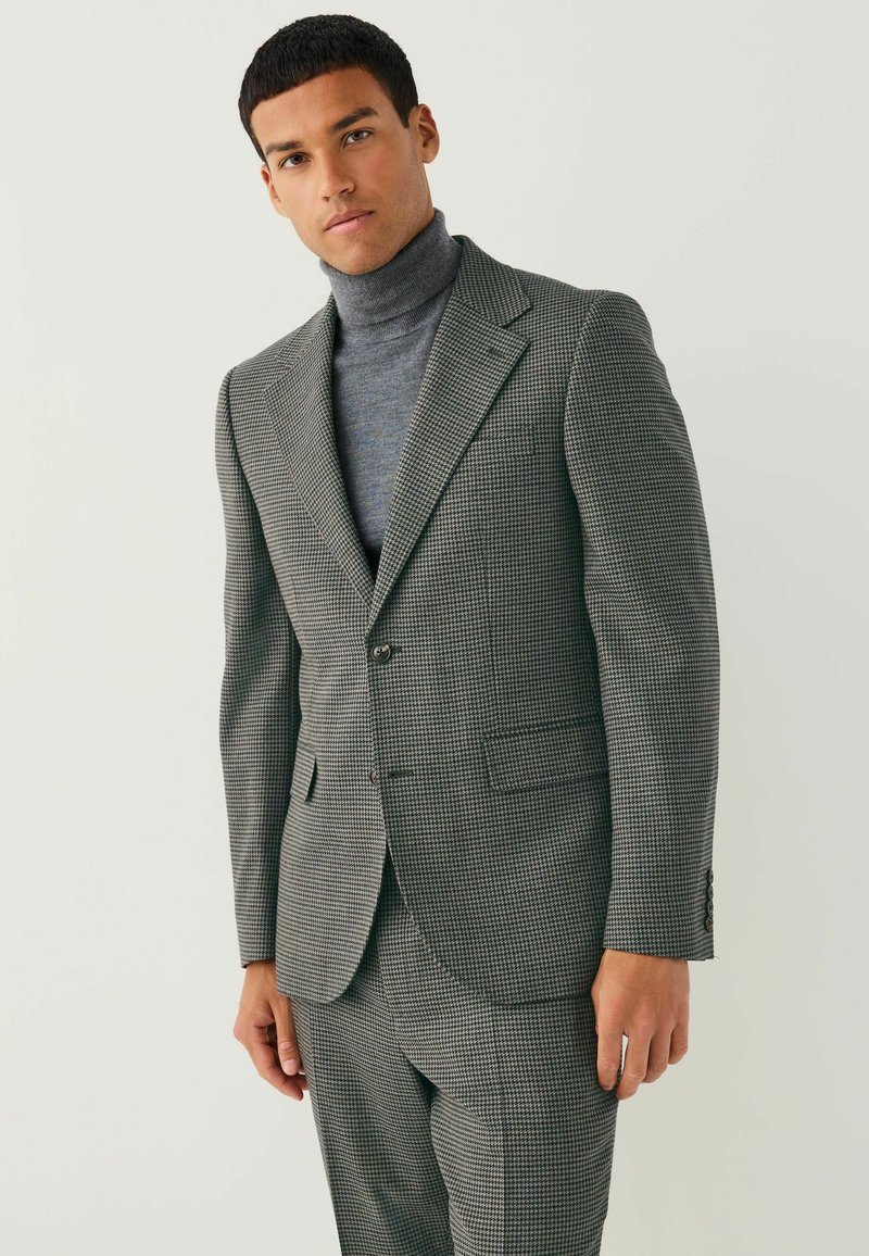 Gray and black houndstooth suit with a structured blazer and matching trousers, worn over a dark turtleneck, showcasing clean lines and tailored fit.