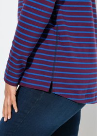 T-shirt long à manches bordeaux avec des rayures horizontales bleues, présentant des fentes sur les côtés et un ourlet qui s'incurve légèrement sur les côtés. Jean bleu foncé.