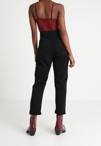 Mustat korkeavyötäröiset suorat housut, yhdistettynä viininpunaisiin kiiltonahkaisiiin nilkkureihin. Pitsinen kokopuku, jossa ohuet olkaimet.