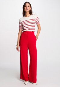 Pantalons larges rouges à taille haute, associés à un haut à manches courtes blanc et rouge à rayures. Présente un détail subtil de bouton sur l'épaule.