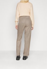 Pull beige, pantalon marron à carreaux taille haute, coupe ajustée, tissu texturé, associé à des chaussures noires à semelles épaisses.