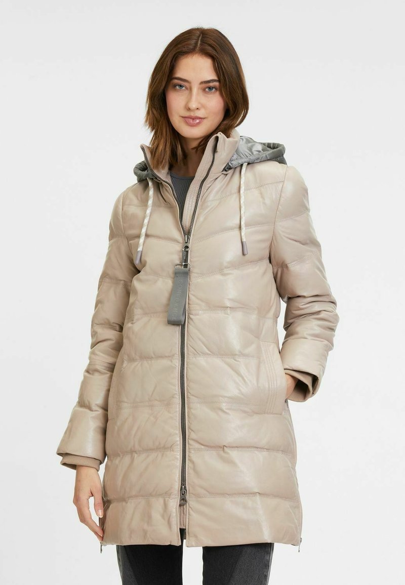 Cappotto puffer beige con texture lucida, maniche lunghe, cappuccio grigio e chiusura frontale con zip; presenta tasche laterali e un motivo trapuntato orizzontale.