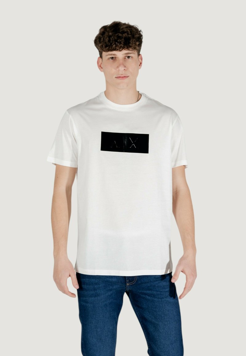 T-shirt bianco in cotone con un logo rettangolare nero sul davanti, maniche corte e un design a taglio dritto, abbinato a jeans in denim blu.