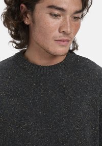 Dunkelgrauer Strickpullover mit einem gerippten Kragen, der durchgängige mehrfarbige Einschlüsse in Blau, Gelb und Orange im Gewebe aufweist.