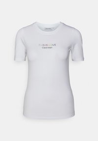 Bílý tričko s krátkým rukávem Calvin Klein s textem "TOTO JE LÁSKA" v duhových barvách a menším logem "Calvin Klein" níže.