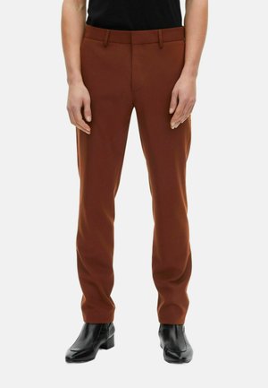 Bruine op maat gemaakte broek met een gladde textuur, slim fit en riemlussen, gecombineerd met zwarte enkellaarsjes. Voorkanten zijn zichtbaar.
