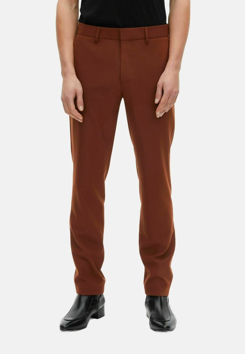 Brune skræddersyede bukser med en glat tekstur, slim fit og bæltestropper, parret med sorte ankelstøvler. Forlomme synlige.