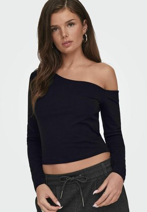 Top nero a maniche lunghe e scollo off-the-shoulder, realizzato in tessuto morbido, con un design aderente e lunghezza cropped, abbinato a pantaloni grigi a fantasia.