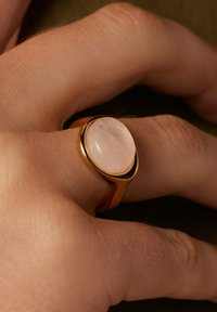 Gouden ring met een gladde rozenkwarts cabochon. De zetting is rond, met een gepolijste oppervlakte en een eenvoudig, minimalist design.