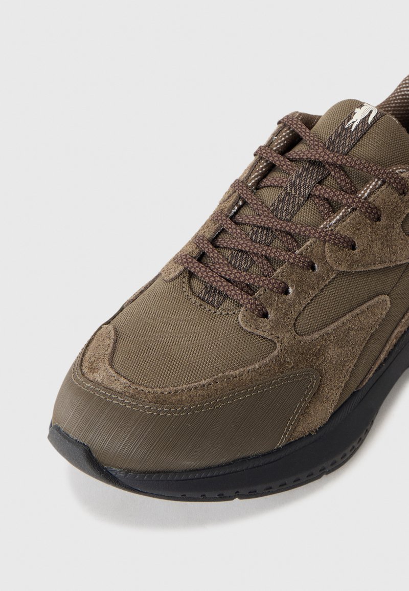 Brauner Sportschuh aus einer Kombination von glattem Stoff und Wildleder, mit strukturiertem Mesh-Obermaterial und dunkler Sohle mit detaillierter Naht.