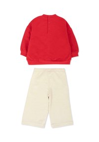 Czerwona bluza z wysokim kołnierzem i zapięciem na guziki z tyłu, zestawiona z kremowymi, luźnymi spodenkami o długości do kolan.
