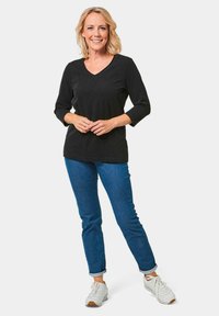 Zwarte, lange mouwen V-hals top gecombineerd met blauwe jeans en witte sneakers. De jeans zijn opgerold bij de boorden en de top heeft een gladde textuur.