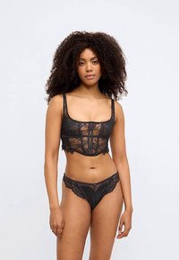 Black lace lingerie set featuring a floral pattern, adjustable straps, structured bodice, and a matching sheer brief with lace accents.