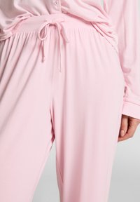 Lichtroze pyjama set met een trekkoord in de taille, lange mouwen en een knoopsluiting bovenkant. Zachte stof met een gladde textuur, ontspannen pasvorm.