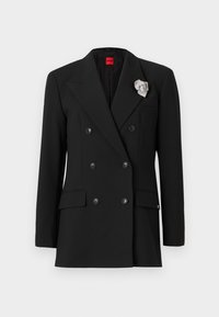 Blazer nero doppiopetto con ampie rever, due tasche frontali e un accento di spilla argentata sul rever. Tessuto dalla consistenza liscia.