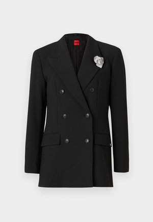 Black double-breasted blazer with large lapels, two front pockets, and a silver brooch accent on the lapel. Smooth fabric texture.
