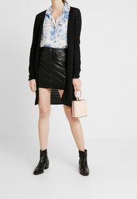 Cárdigan de punto negro, blusa de teñido anudado azul, falda mini de piel negra, botas negras de tobillo y un pequeño bolso de mano con estampado de cocodrilo rosa.