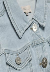 Svetlo modra denim jakna z izostrenim ovratnikom, vidnim šivanjem in srebrnimi pritrdilnimi gumbi. Ima žep na prsih z zaobljenimi pokrovi.