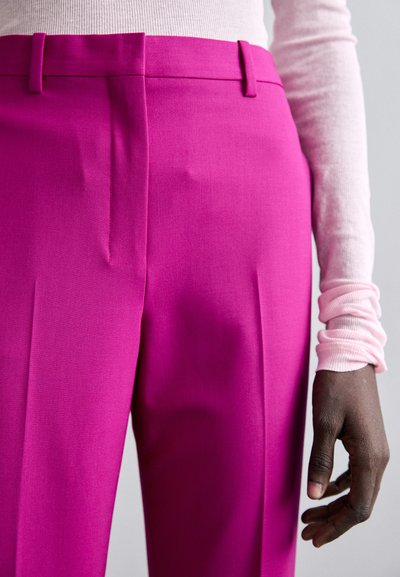 Magentan muoti-housut, joiden pinnalla on sileä tekstuuri, sisältävät kaksi etupleattiä ja vyölenkit, yhdistettynä vaaleanpunaisiin ribbitekstuuriin pitkähihapaitaan.