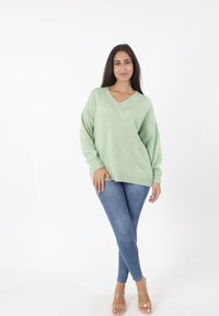 Lichtgroene oversized trui met een V-hals, geribbelde manchetten en zoom, gecombineerd met blauwe skinny jeans en doorzichtige sandalen met hak.