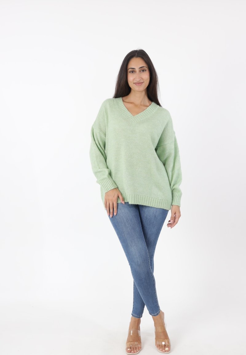 Lichtgroene oversized trui met een V-hals, geribbelde manchetten en zoom, gecombineerd met blauwe skinny jeans en doorzichtige sandalen met hak.