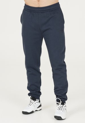 Marina blå sweatpants med elastiskt midjeband, sidofickor och en diskret logodetalj framtill, tillsammans med vita sneakers.