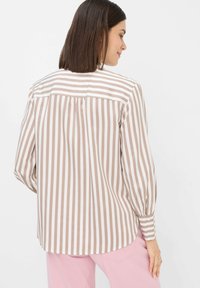 Blusa a righe con colori alternati marrone chiaro e bianco, maniche lunghe con polsini bottone e orlo arrotondato. Dettaglio della piega sul retro visibile.