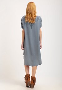 Modré midi šaty s krátkými rukávy, na krku s dekoračním designem, v kombinaci s hnědými kotníkovými botami s třásněmi.