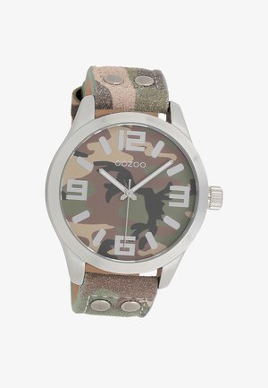 Montre camouflage avec un boîtier en acier inoxydable, grands index horaires blancs et un bracelet en tissu texturé vert et marron avec des clous en métal.