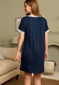 Rochie de noapte bleumarin cu mâneci scurte bordate cu dantelă, având o croială lejeră și un material neted. Privirea din spate evidențiază un design simplu.