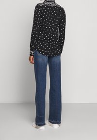 Svart långärmad skjorta med ett vitt bladmönster och detaljerad krage; matchad med ljusblå vida jeans och vita sneakers.