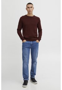 Burgundy knitted sweater with a crew neckline, paired with light blue denim jeans and black sneakers featuring white soles.