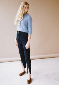 Maglione azzurro chiaro a lavorazione a trecce, pantaloni scuri a vita alta con spacchi all'orlo e scarpe marroni slip-on. Design semplice e testurizzato.