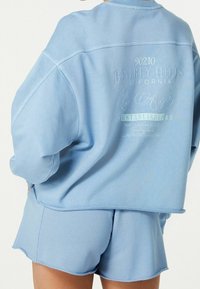 Set composto da felpa azzurro chiaro e pantaloncini. La felpa presenta un motivo testuale in rilievo con "Beverly Hills" e "Established 88" sulla schiena.