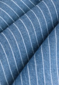 Tessuto di denim con uno sfondo blu strutturato, caratterizzato da sottili strisce verticali bianche, che mette in mostra la trama e il contrasto di colore.