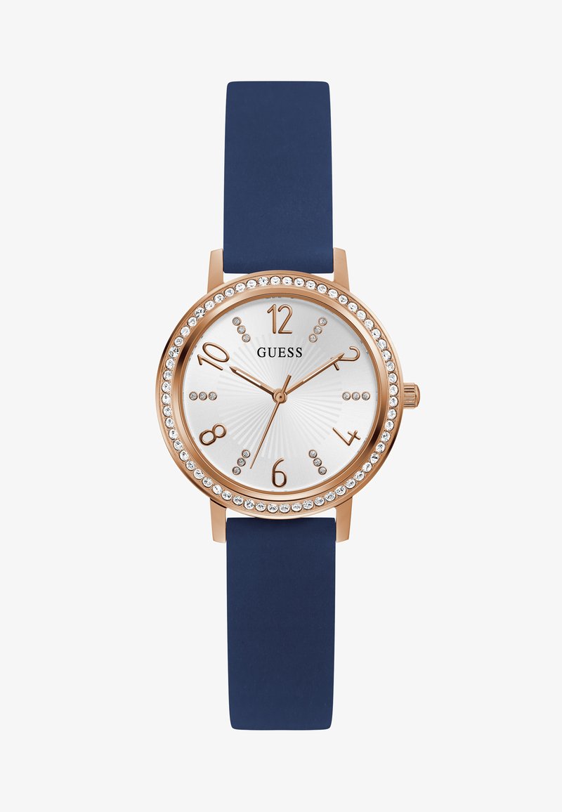 Rózsa arany színű óra kerek, fehér textúrált számlappal, tengerészkék szilikon szíjjal és kristály díszítésekkel az üvegkeret körül. Nagy méretű számokkal és mutatókkal rendelkezik.