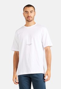 Weißes Baumwoll-T-Shirt mit kurzen Ärmeln, Rundhalsausschnitt und mittig aufgedrucktem Logo. Glatte Textur und entspannter Schnitt.